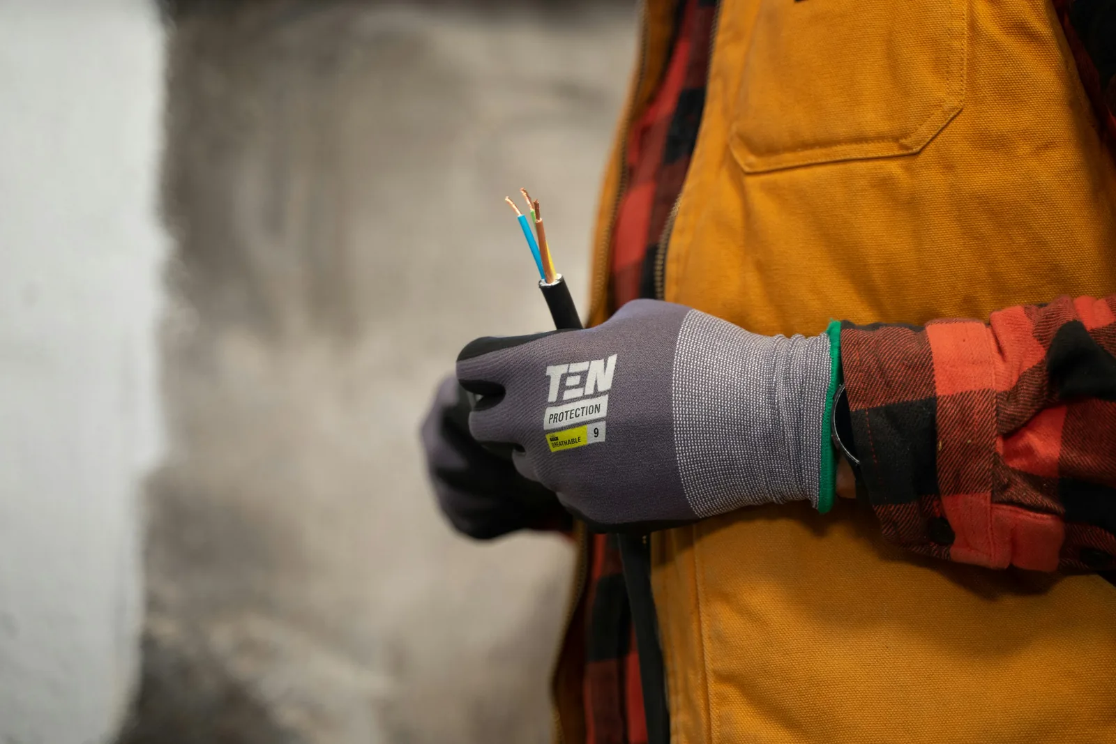 Gloved hands holding an electrical cable, with tools and workwear ready for the job.